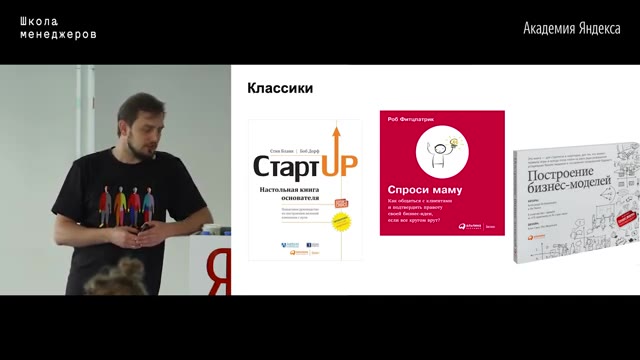 01:32:00 — Тот же слайд «Классики» с тремя книжными обложками, преподаватель смотрит вниз, стоя у